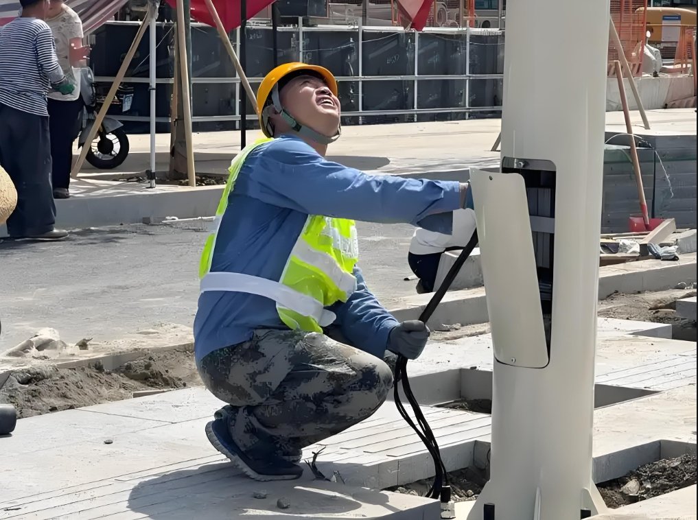 Two electricians in safety gear perform a high-level inspection and maintenance on the wiring of a streetlight, standing on a lift platform and working amidst a network of overhead cables in an urban environment.